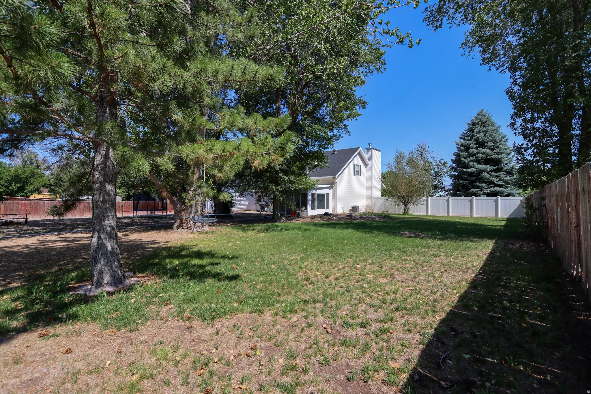 Expansive backyard featuring a partial wood fence, a partial white vinyl fence, and mature trees providing natural shade