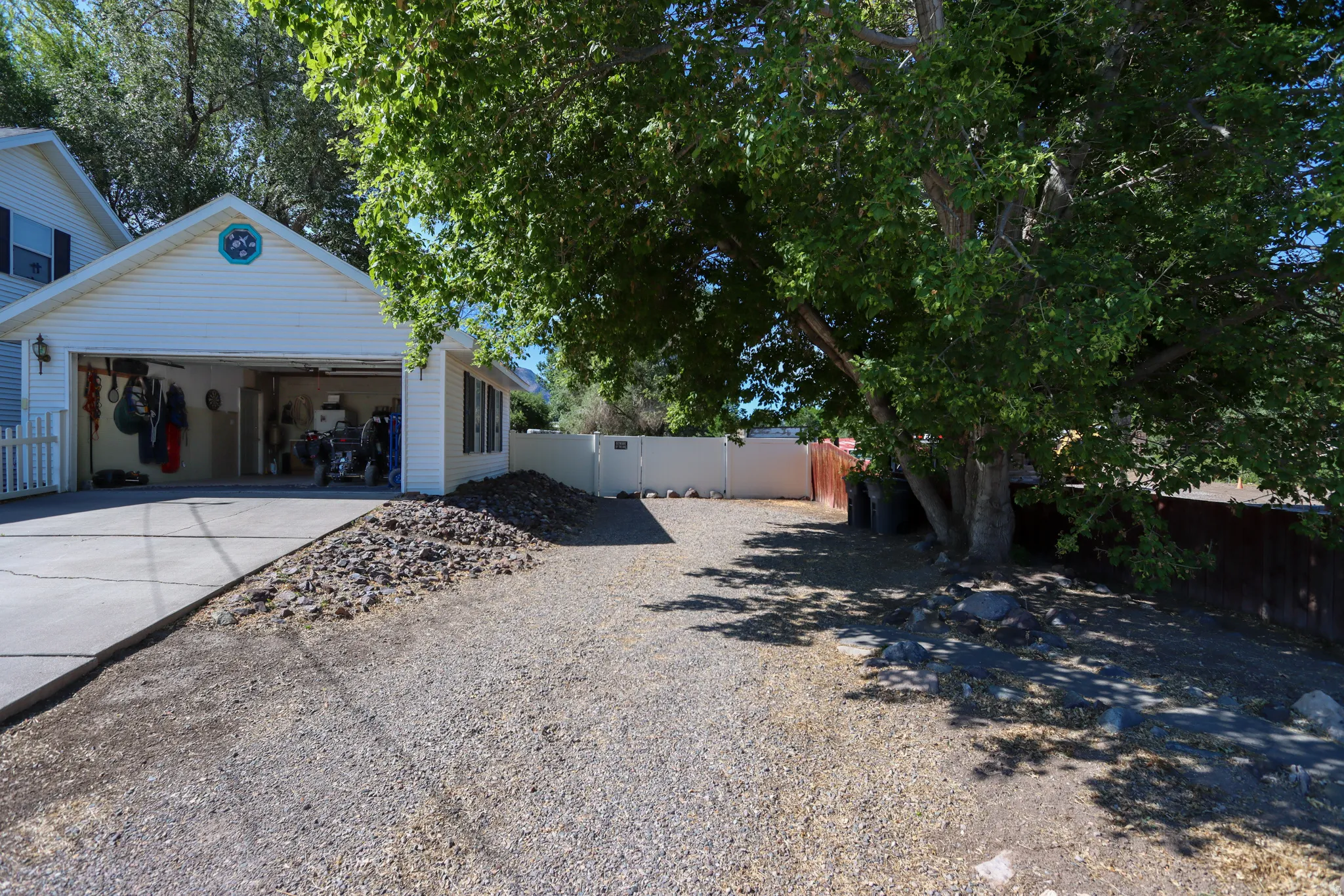 Two-car garage with white vinyl siding, a concrete driveway, and an adjacent gravel parking area