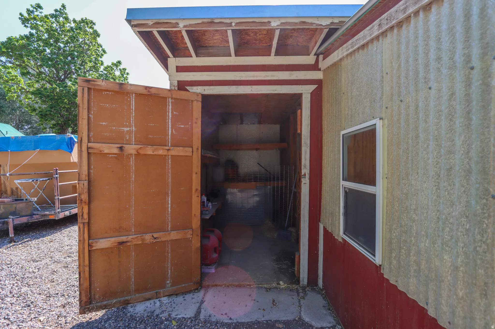 Outbuilding featuring a corrugated metal exterior, red trim accents, and a single-pane window