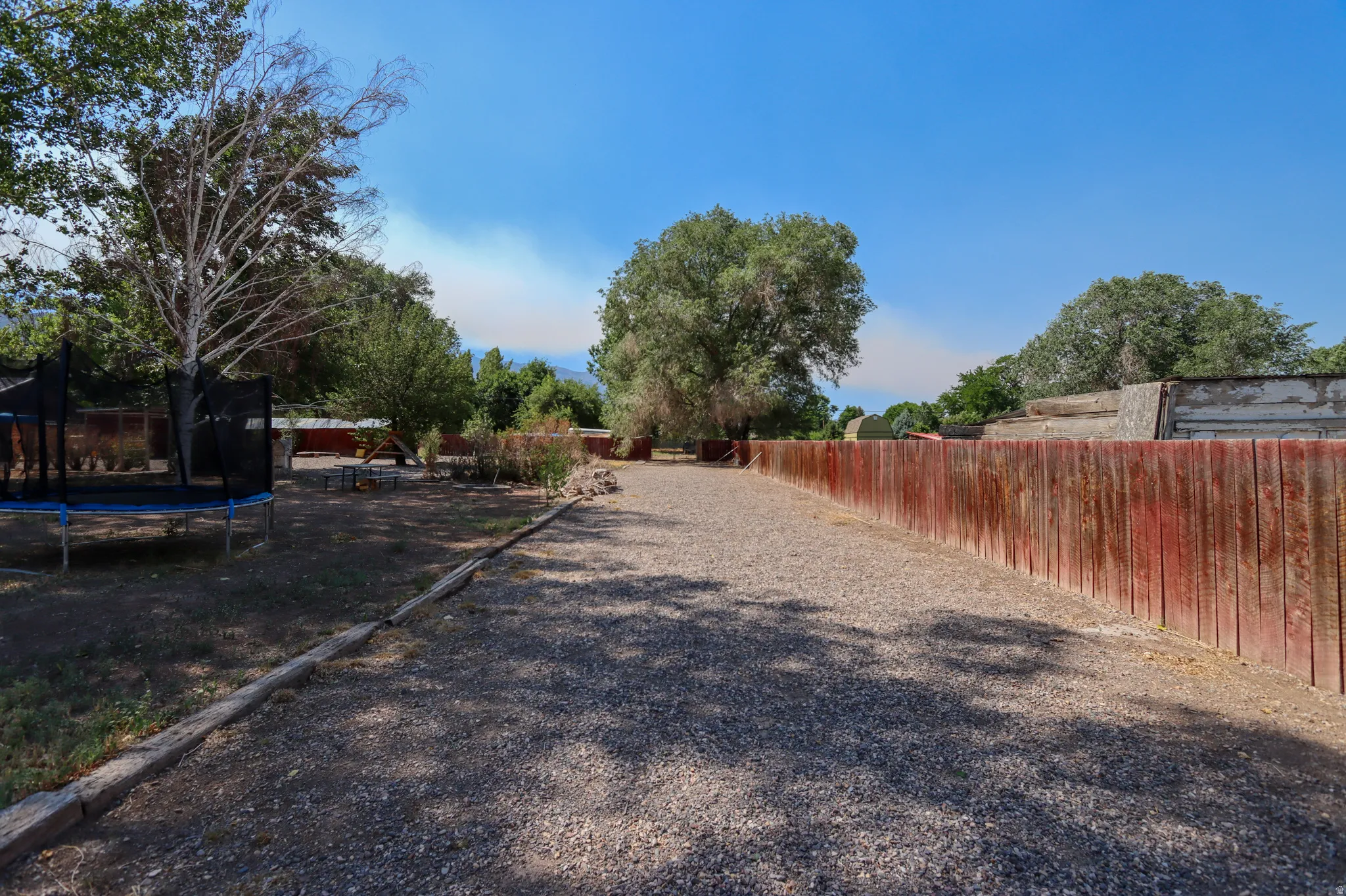Expansive gravel pathway bordered by a red-stained wooden fence and mature trees