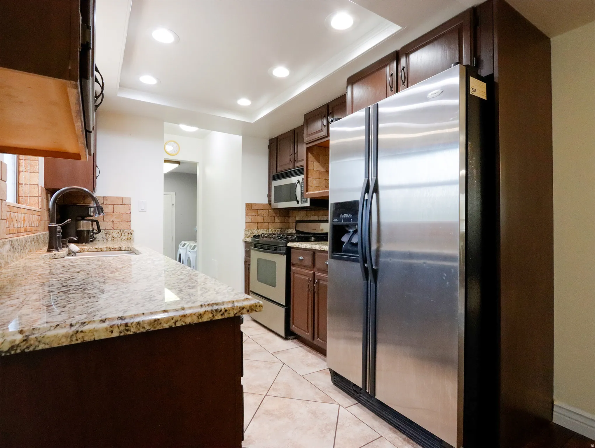 Kitchen featuring warm wood cabinetry, stainless steel appliances, speckled stone countertops, and a brick-patterned tile backsplash