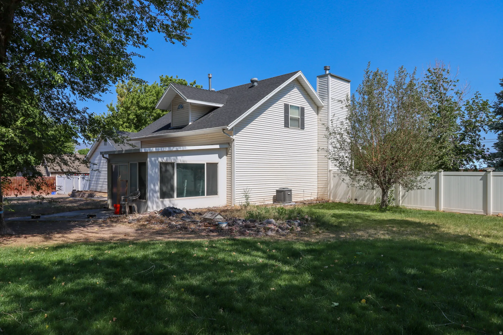 Expansive backyard featuring a manicured lawn, established tree, and a white privacy fence