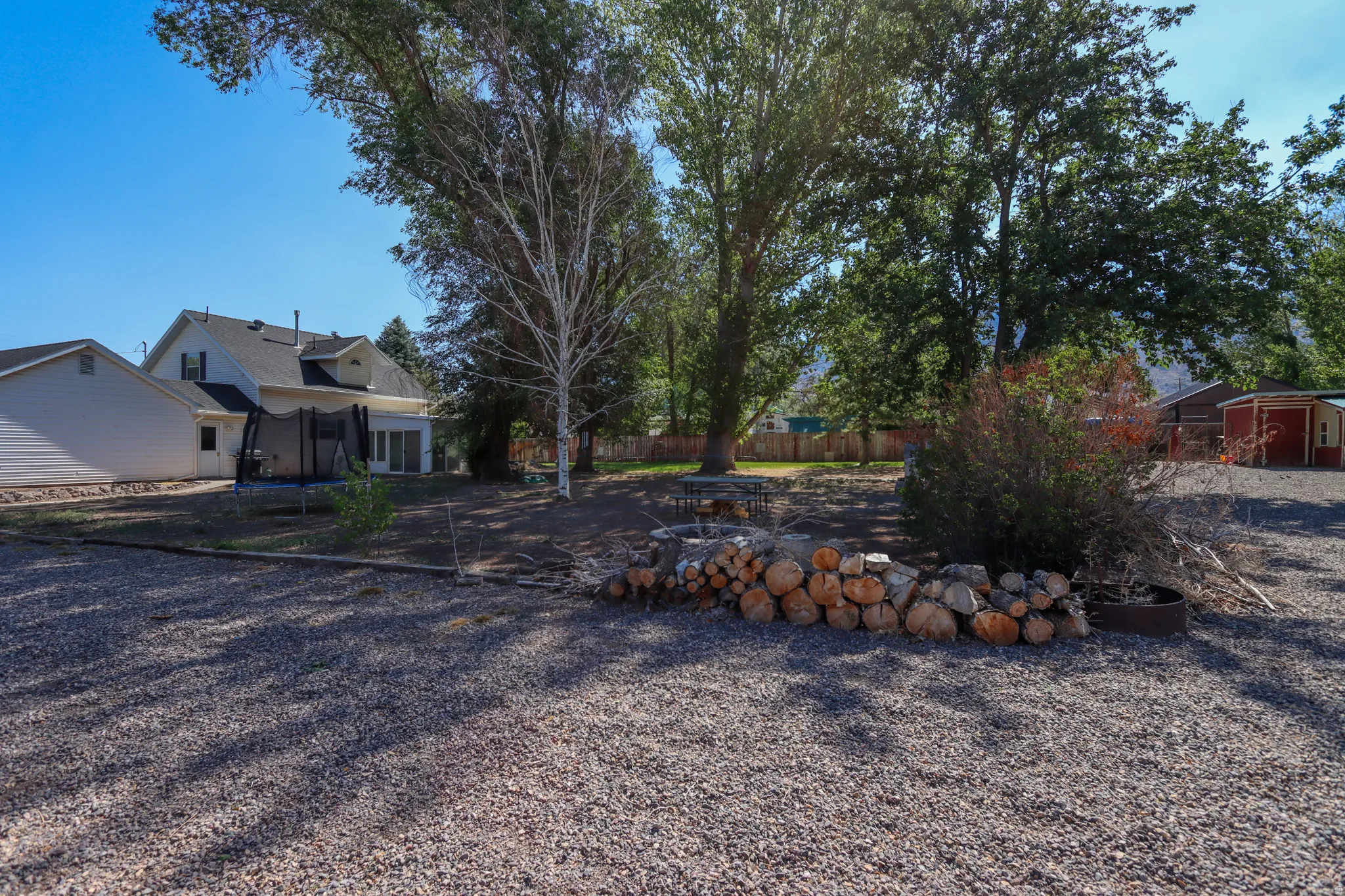 Expansive gravel yard area with mature trees and visible woodpile