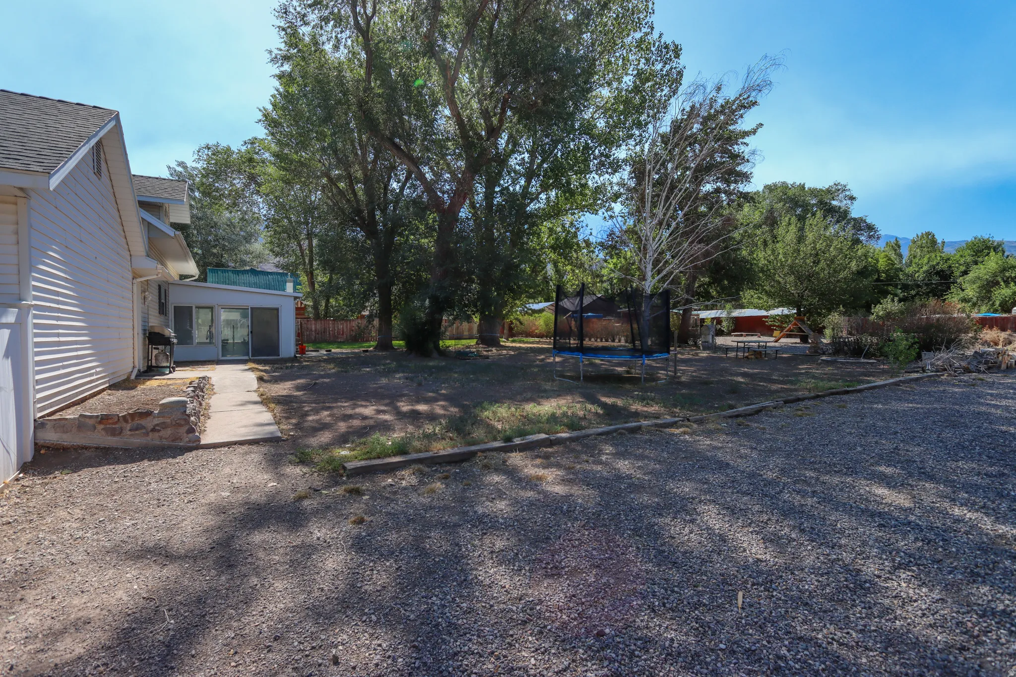 Expansive gravel parking area beside a white-sided residence with a covered patio and sliding glass doors