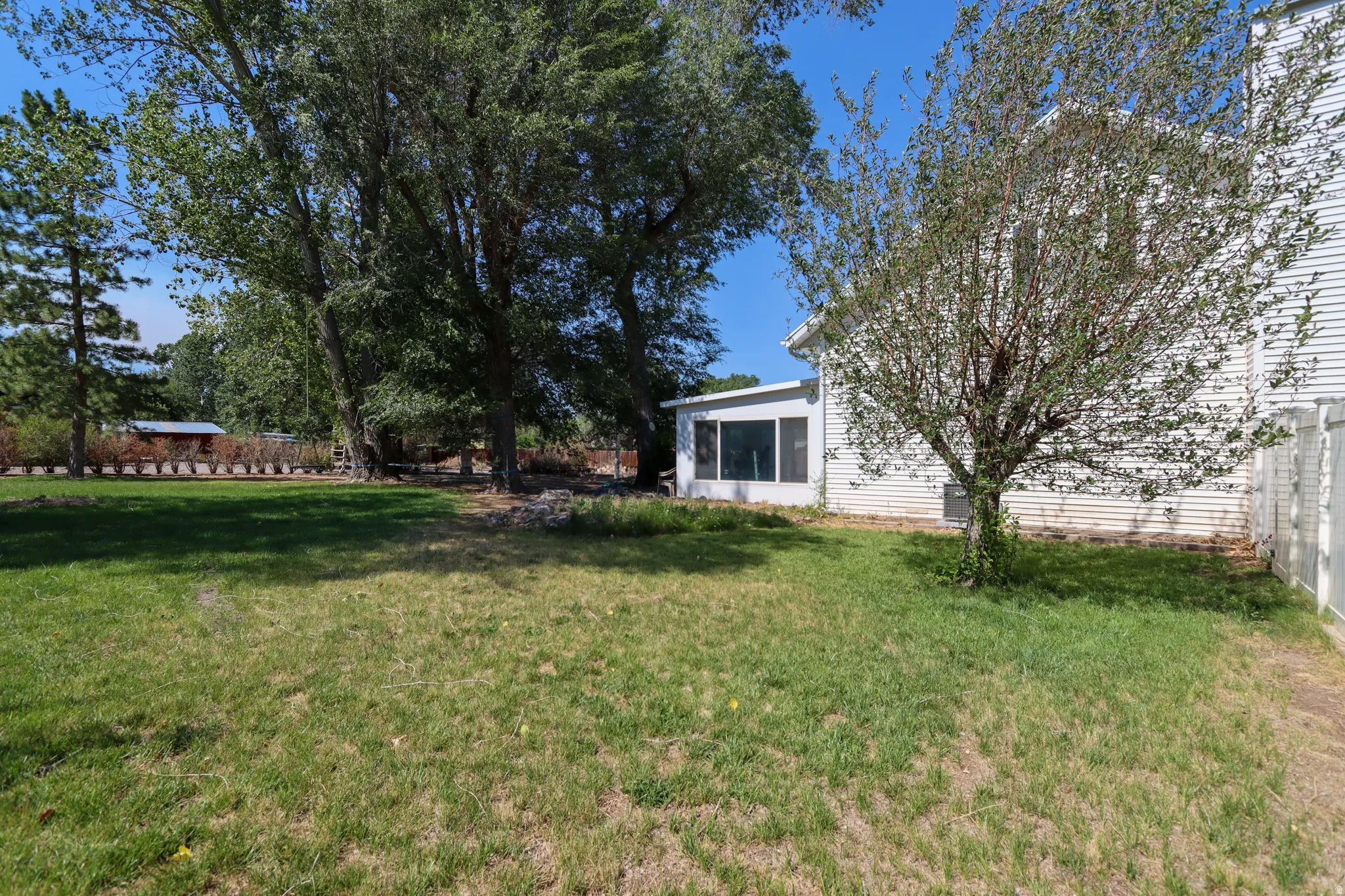 Expansive green lawn area featuring mature trees and a screened-in porch with white siding