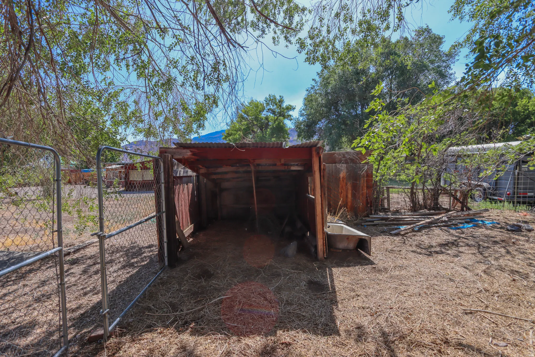 Fenced outdoor area featuring a rustic open-sided structure with a corrugated metal roof