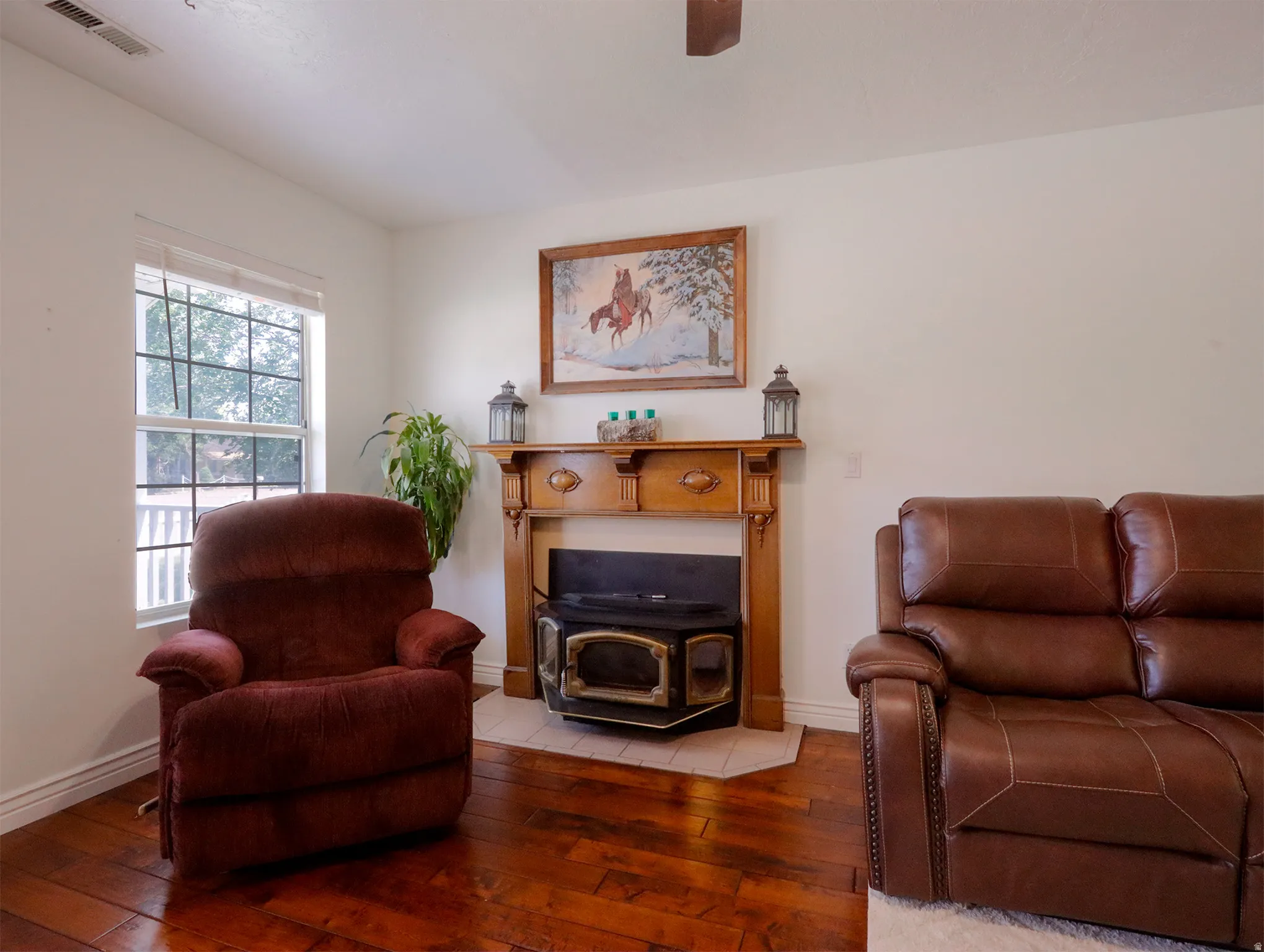 Living area featuring wood-finish flooring, a wood-burning stove with a tile hearth, and a decorative wood mantelpiece