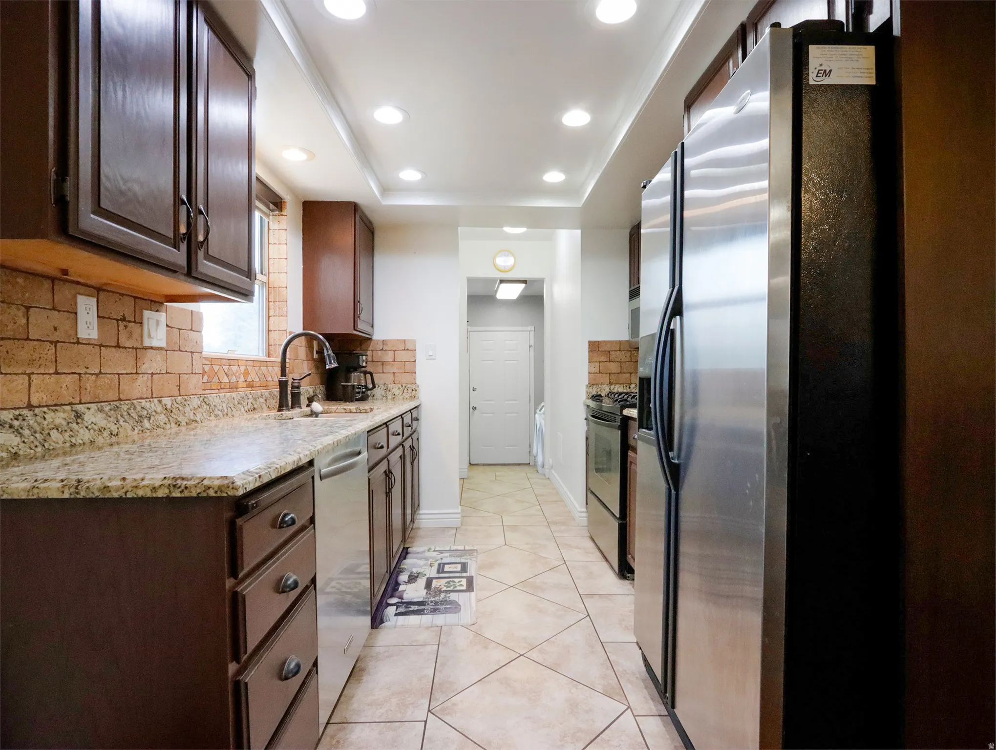 Kitchen featuring recessed lighting, dark wood cabinetry, light-toned countertops, a brick-style backsplash, and stainless steel appliances