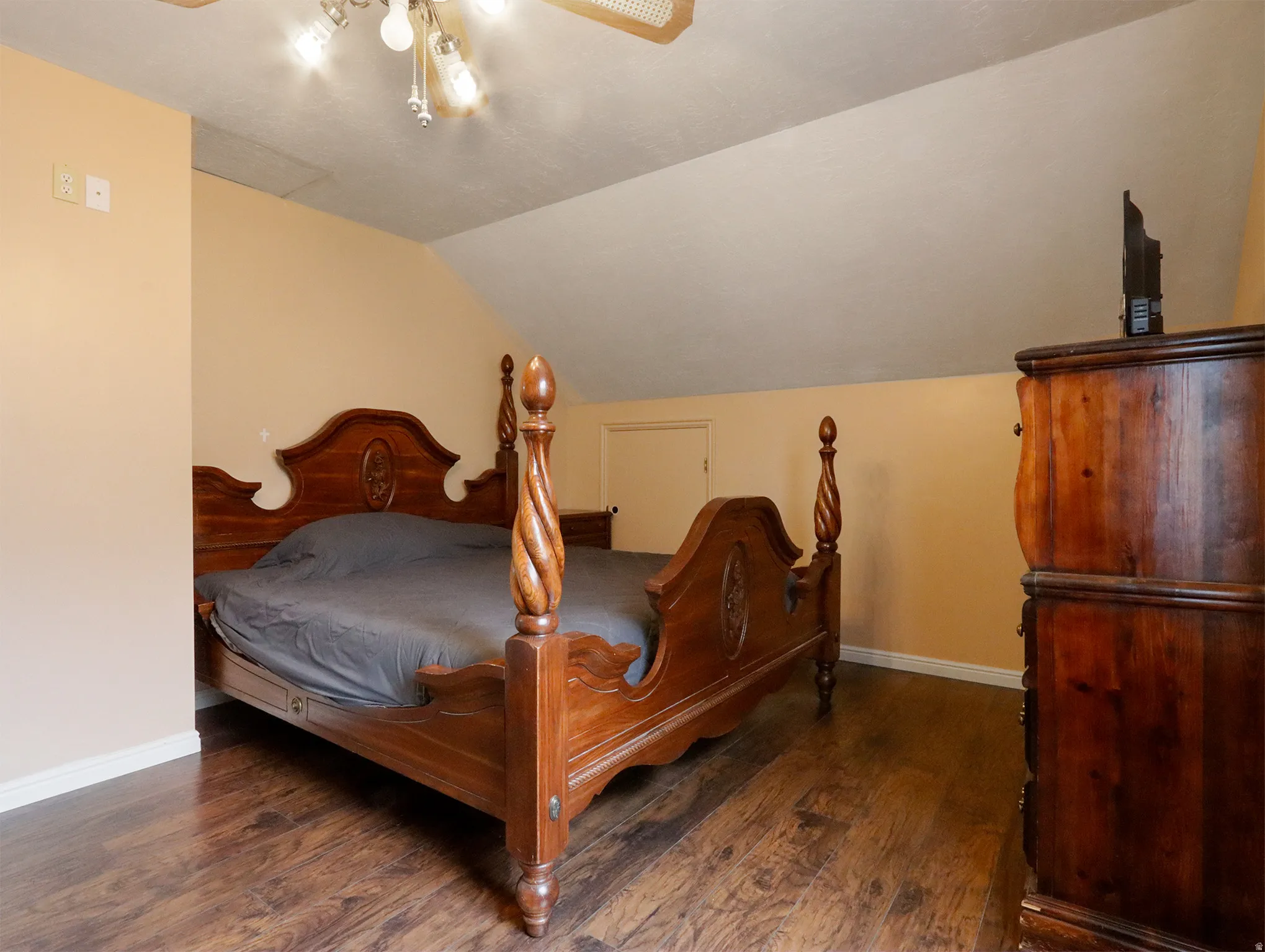 Wood-finish flooring with baseboard trim, complemented by a sloped ceiling and warm-toned walls