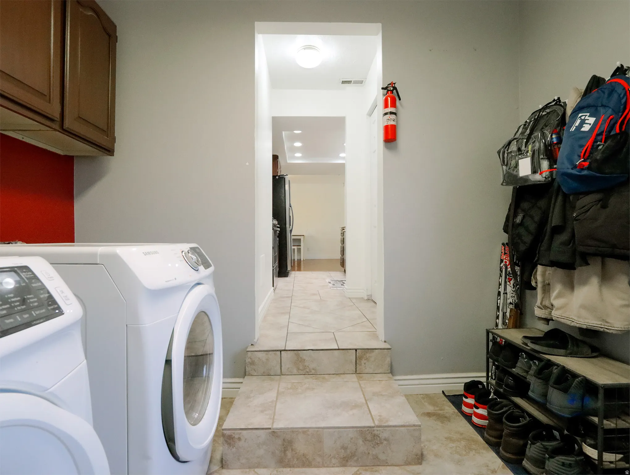 Laundry area featuring ceramic tile flooring, upper wood cabinetry, and a vibrant red accent wall