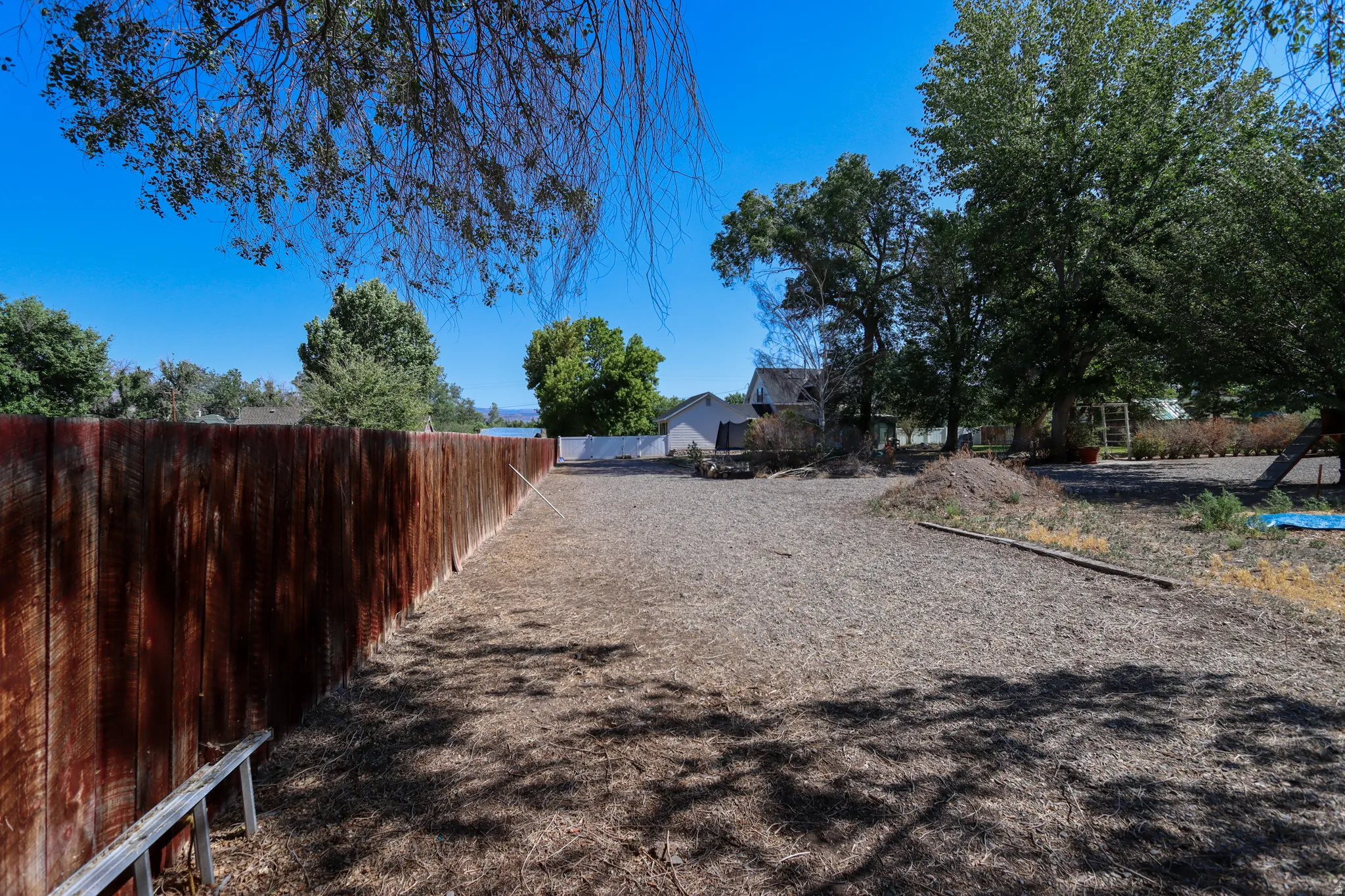 Expansive outdoor space featuring a tall privacy fence, mature trees, and a gravel surface