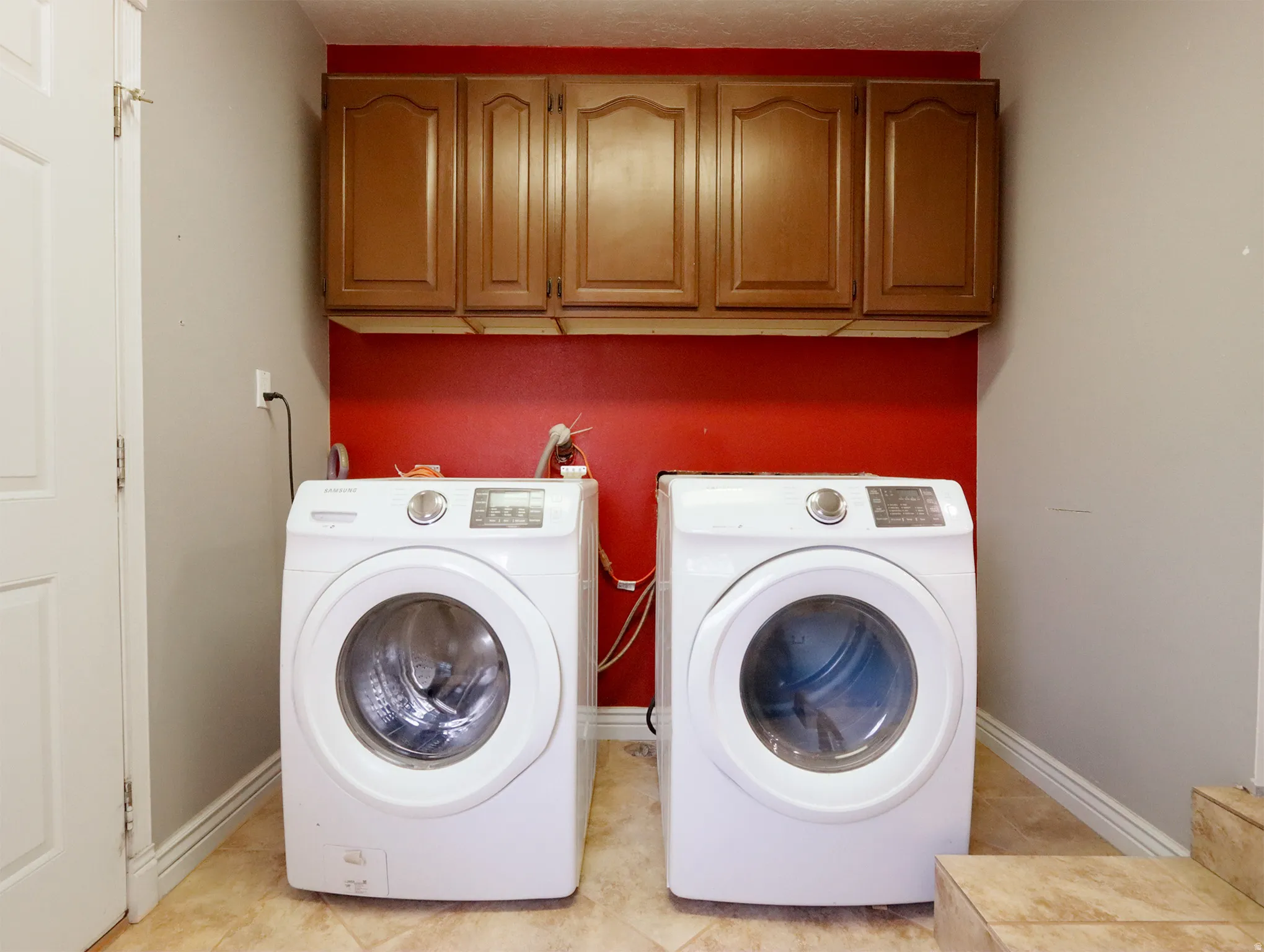 Dedicated laundry area featuring overhead wood-finish cabinetry, a red accent wall, and ceramic tile flooring