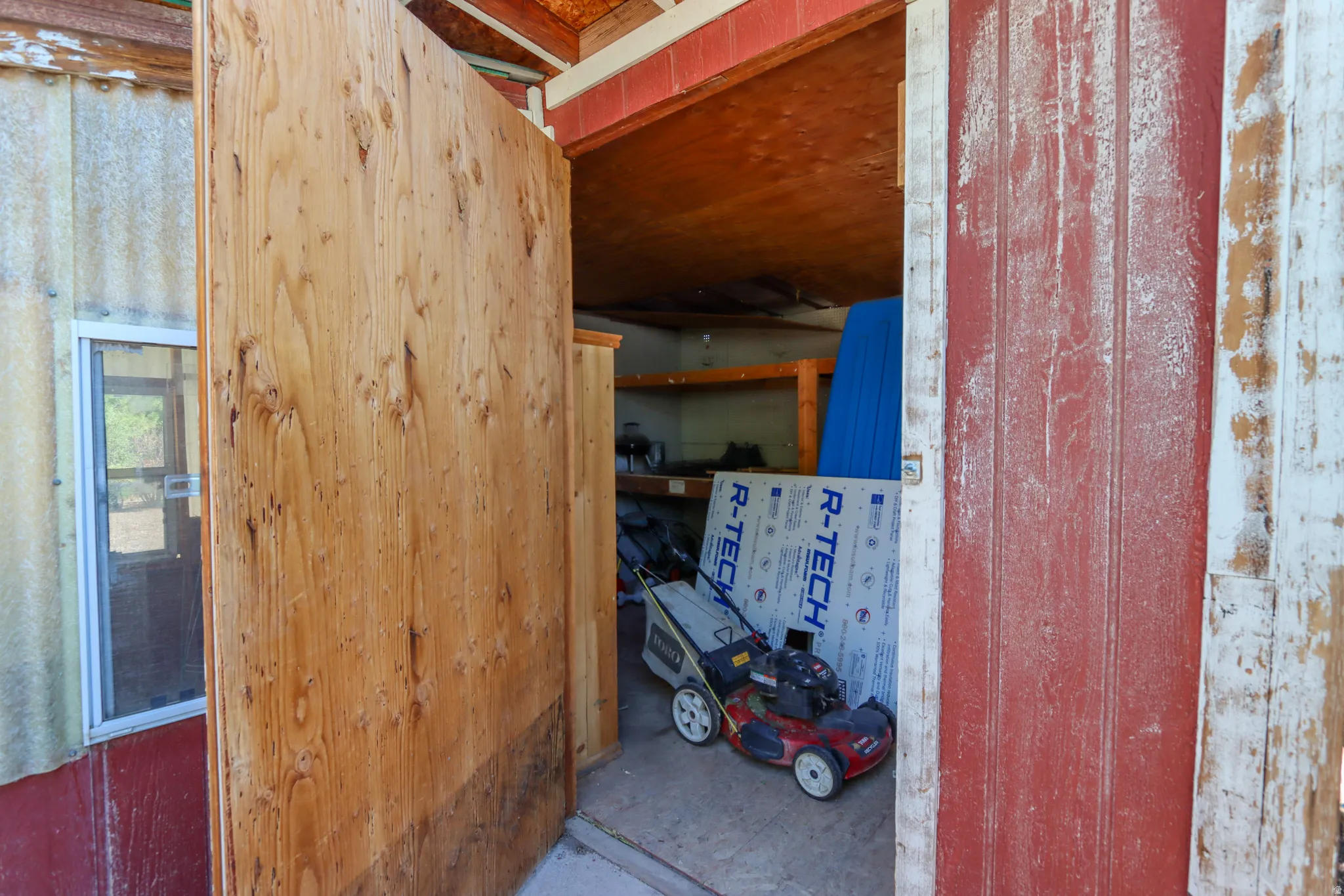 Interior storage area featuring exposed wood framing, an open doorway, and a small window with a white frame