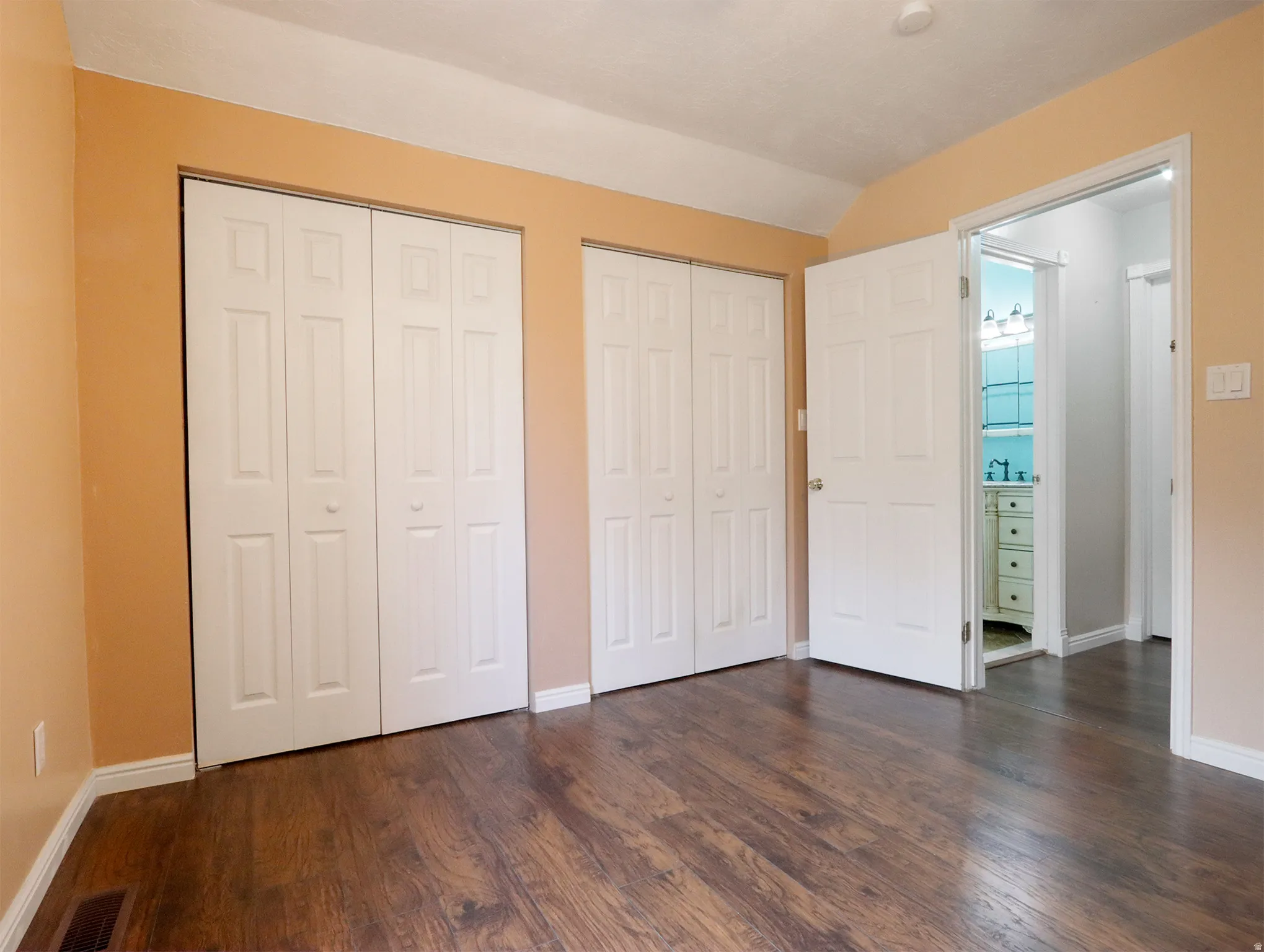 Interior room featuring wood-finish flooring, two sets of white bi-fold closet doors, and light tan wall paint