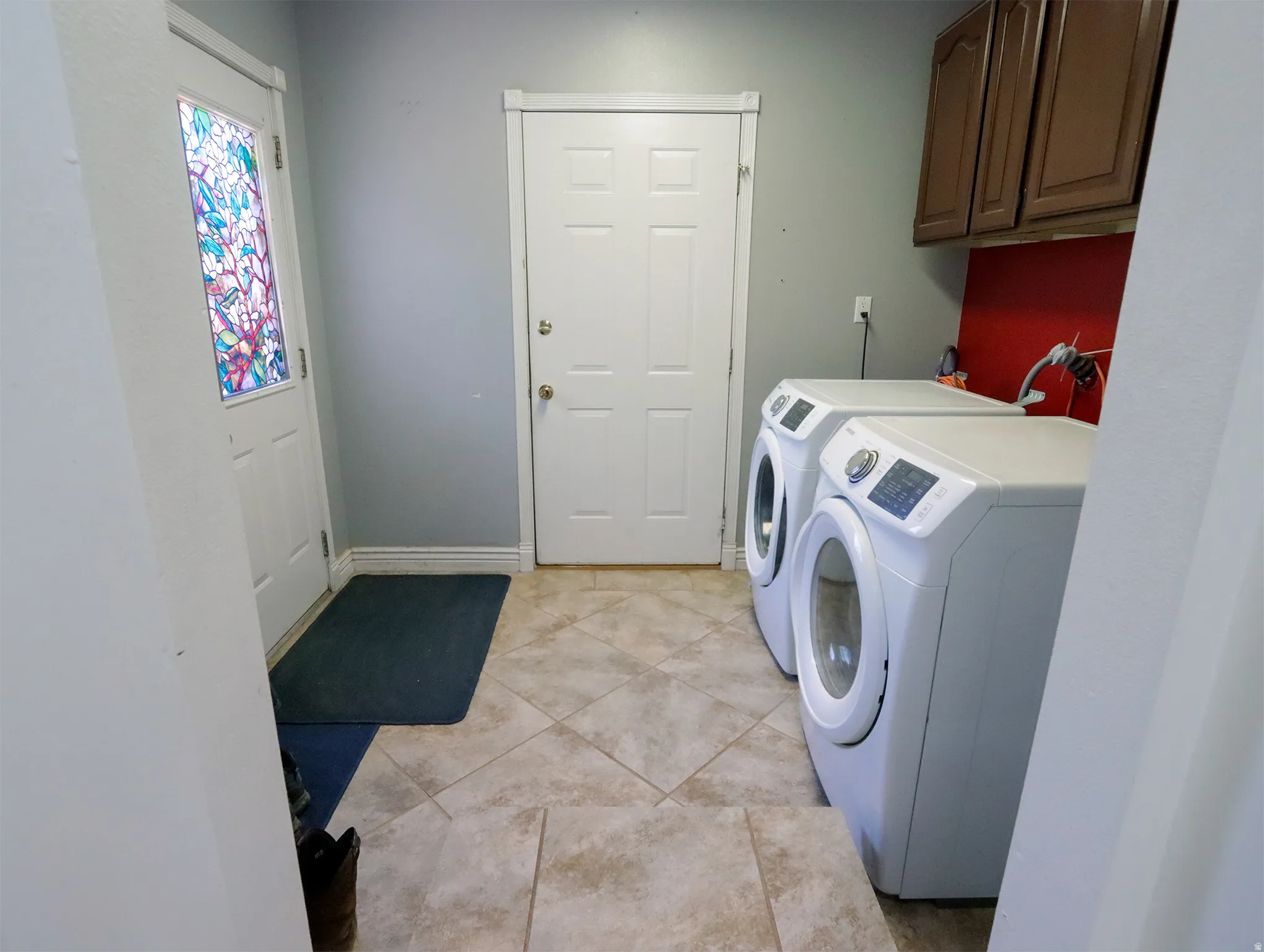 Laundry area featuring ceramic tile flooring, upper cabinetry, and a red accent wall