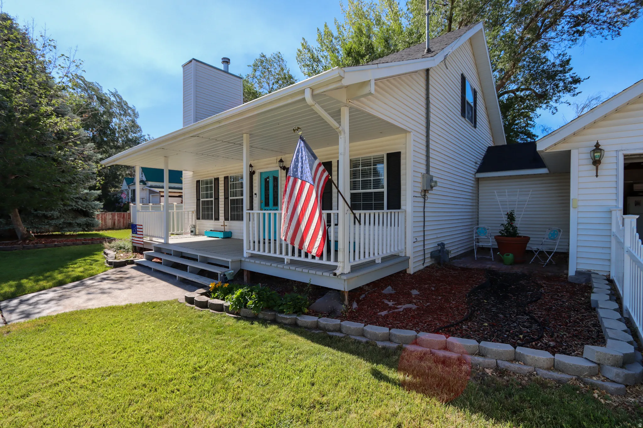 White siding exterior with a covered porch featuring white railings, a contrasting blue entry door, and dark window shutters
