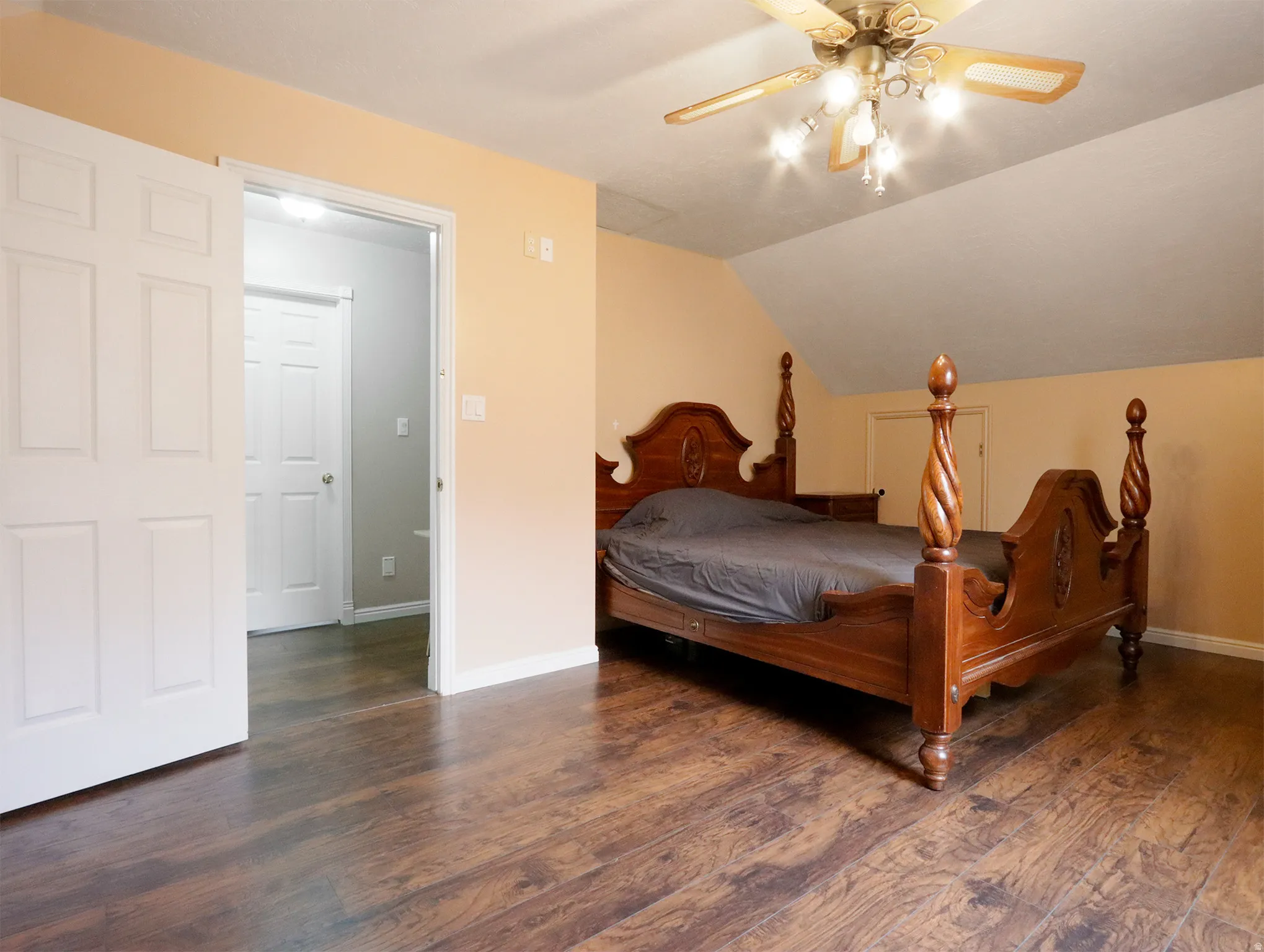 Expansive room featuring wood-finish flooring, a vaulted ceiling, and a ceiling fan with integrated lighting