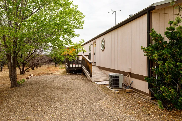 Exterior side profile with a gravel ground cover, established trees, and a raised wooden deck leading to an entry door