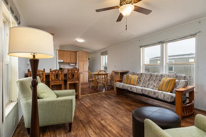 Open concept living area featuring wood-finish flooring, multiple window exposures, a ceiling fan with integrated lighting, and natural wood cabinetry
