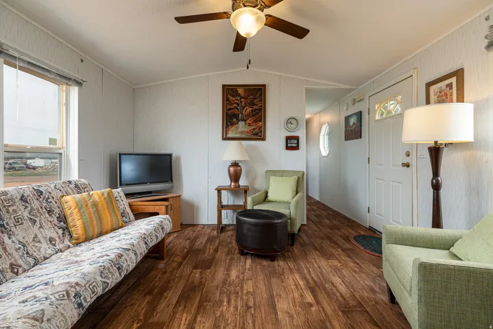 Living area featuring wood-finish flooring, textured wall panels, a ceiling fan with integrated lighting, and a front entry door with decorative glass inserts
