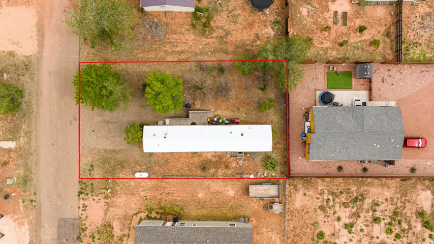 Aerial view of a rectangular lot, outlined in red, featuring a single-story residence with a light-colored roof