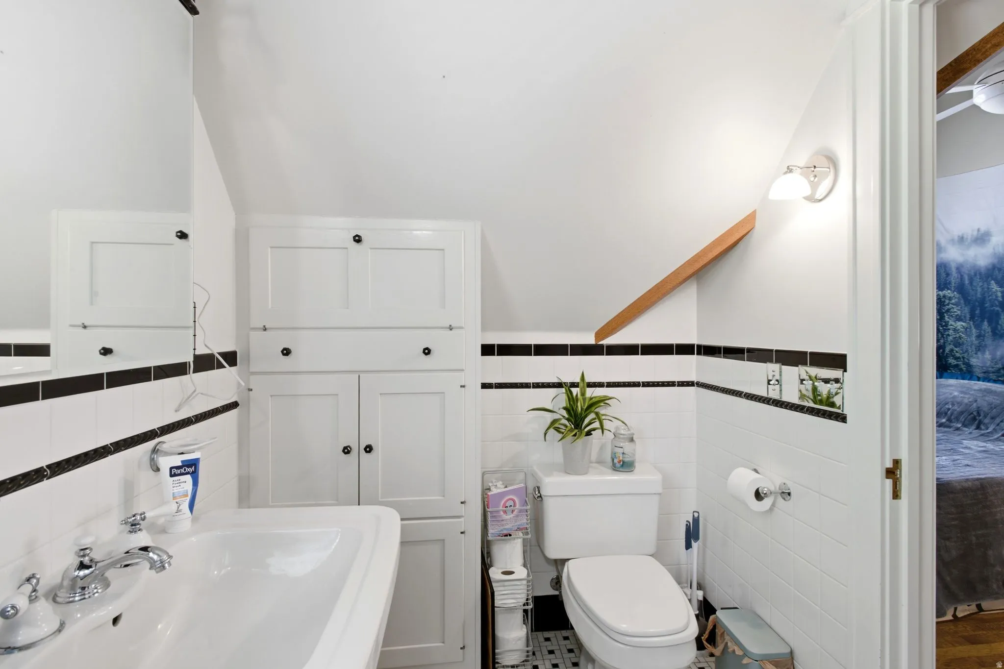 Bathroom featuring a pedestal sink with chrome fixtures, built-in white cabinetry, and white subway tile with black accent bands