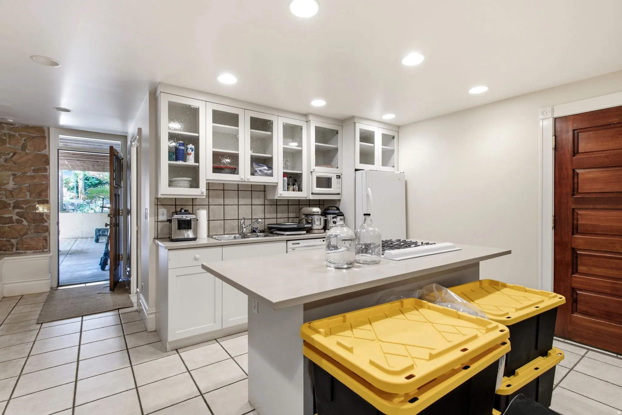 Kitchenette featuring white cabinetry with glass-front uppers, a light-toned countertop island with a built-in cooktop, and recessed lighting