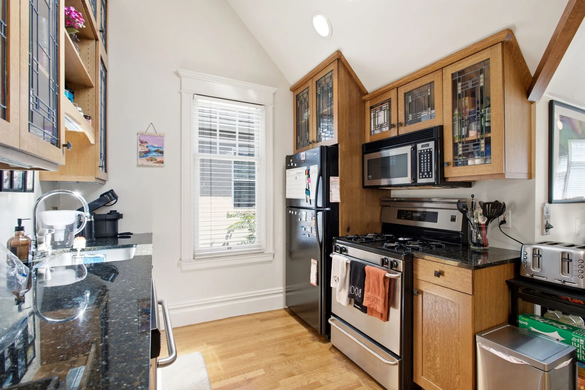 Kitchen featuring wood-finish cabinetry with glass inserts, black speckled countertops, and stainless steel appliances including a range and microwave