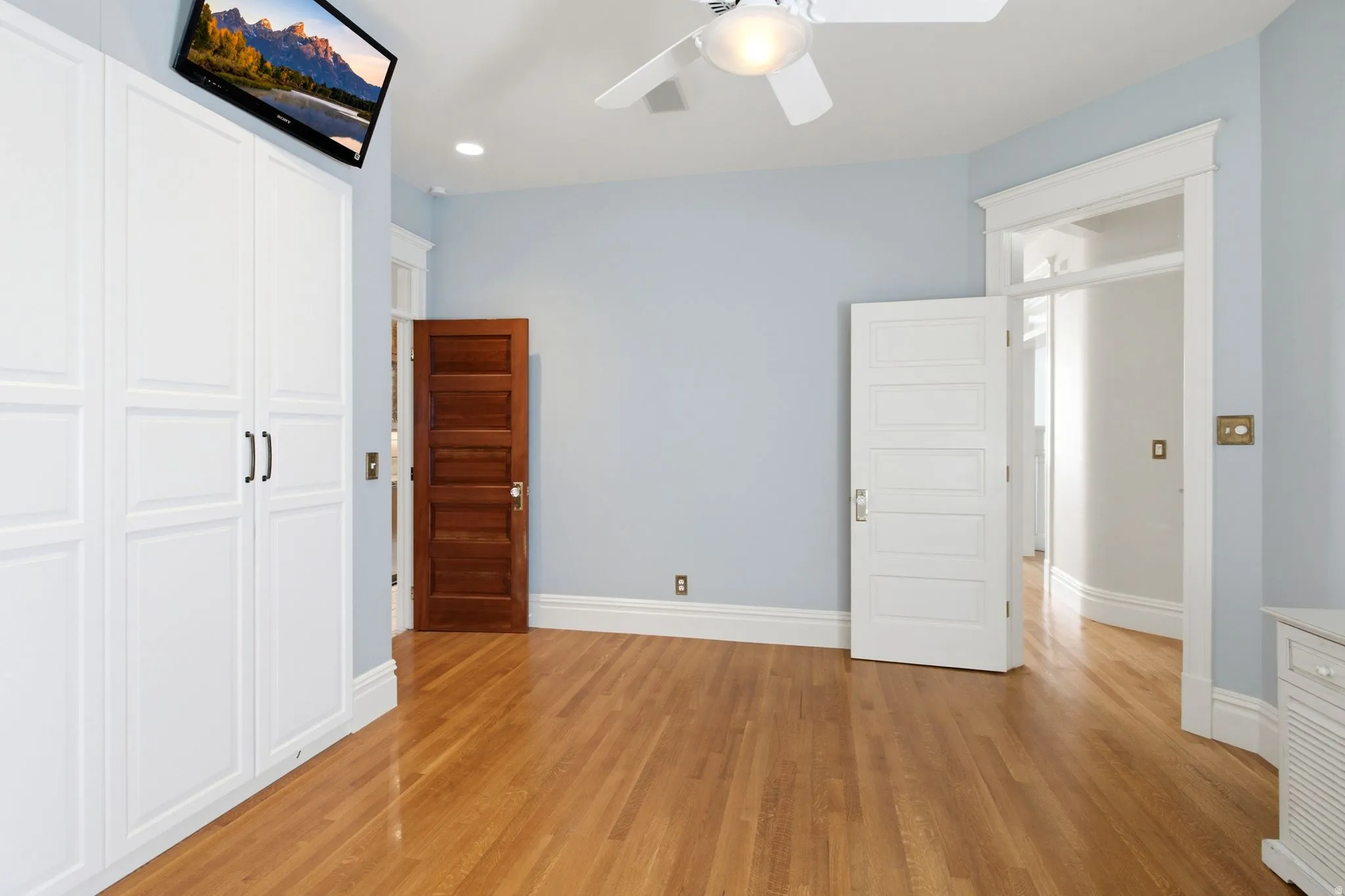Light-filled interior featuring wood-finish flooring, built-in white panel cabinetry, a ceiling fan, and architectural trim details