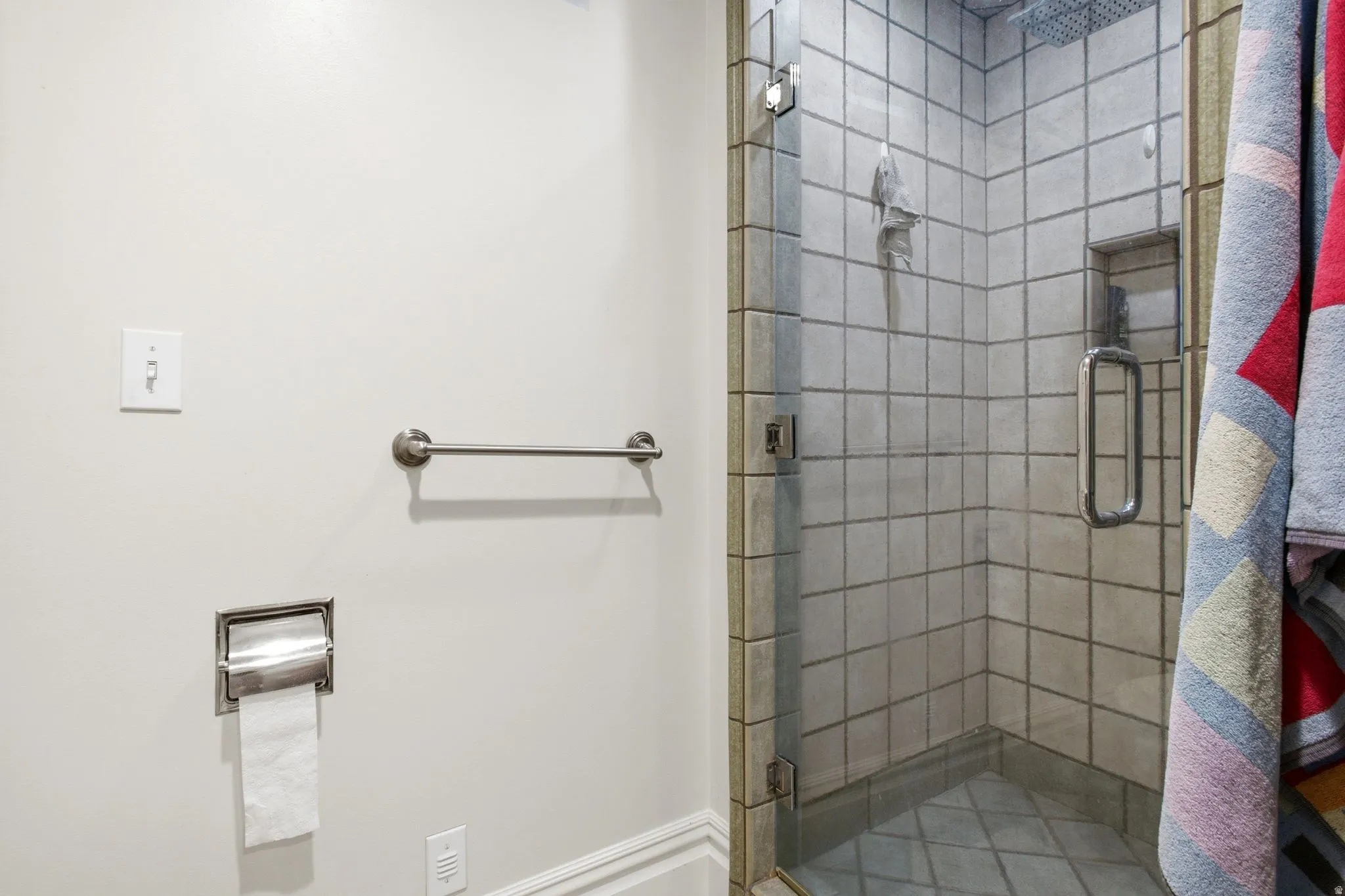 Glass-enclosed shower with square wall tiling, a built-in shelf, and a rain shower head