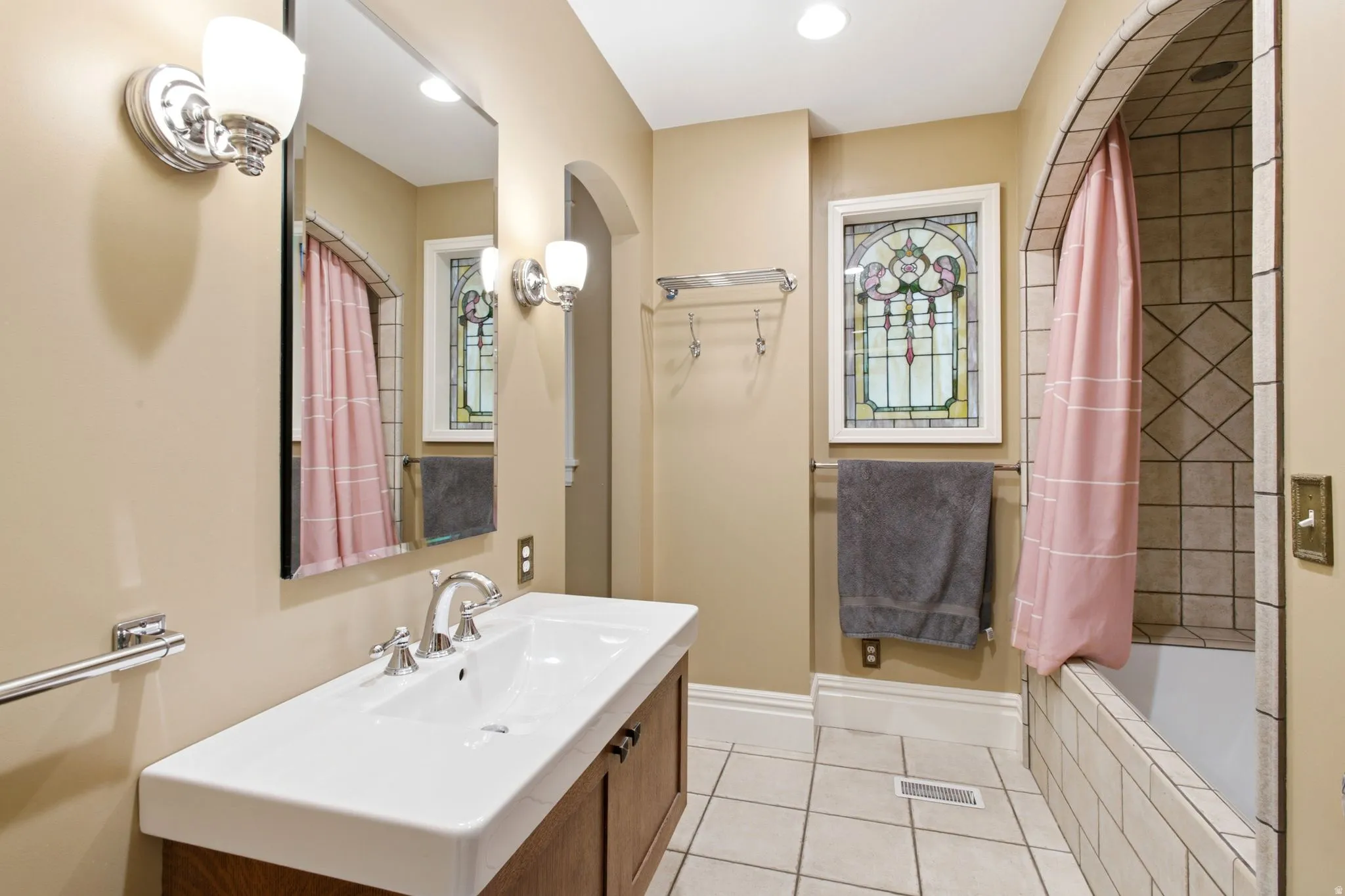 Bathroom featuring a decorative stained-glass window, a wood-finish vanity with an integrated sink, and an arched tile shower surround