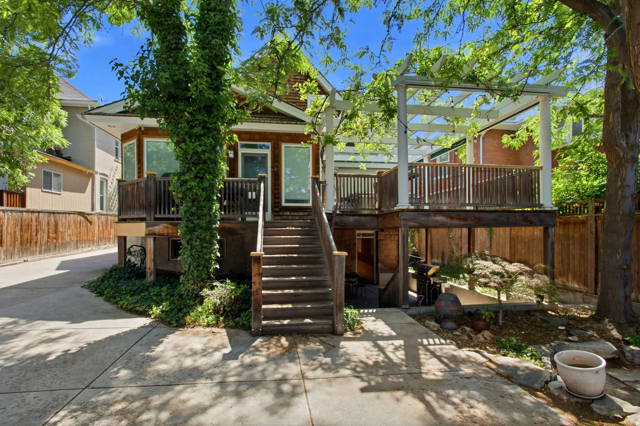 Expansive outdoor living space featuring a multi-level wood deck, white pergola, and mature trees