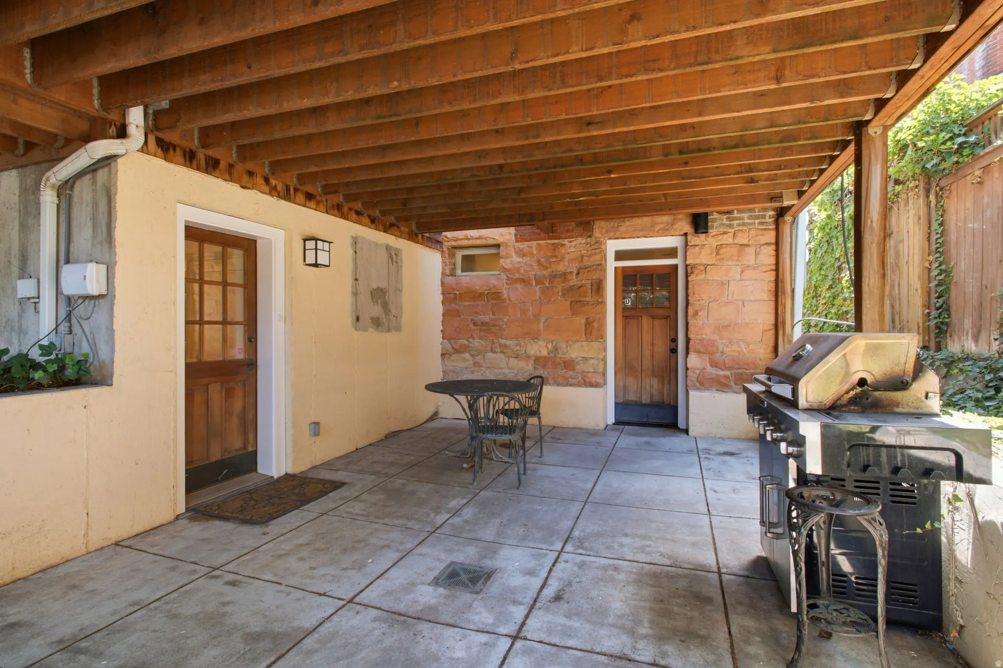 Covered patio area featuring a concrete slab, exposed wood beam ceiling, and two wood-paneled doors with glass inserts