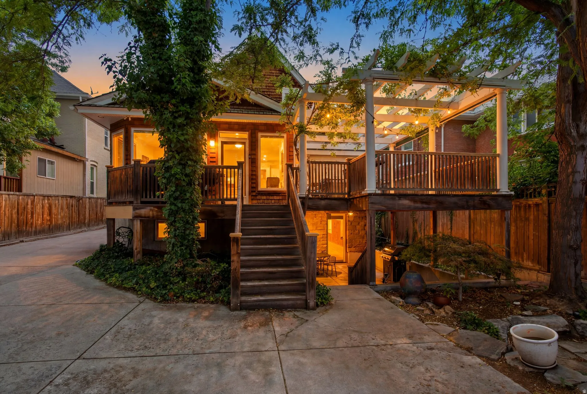 Multi-level rear deck with a white wood pergola, string lighting, and wood railings