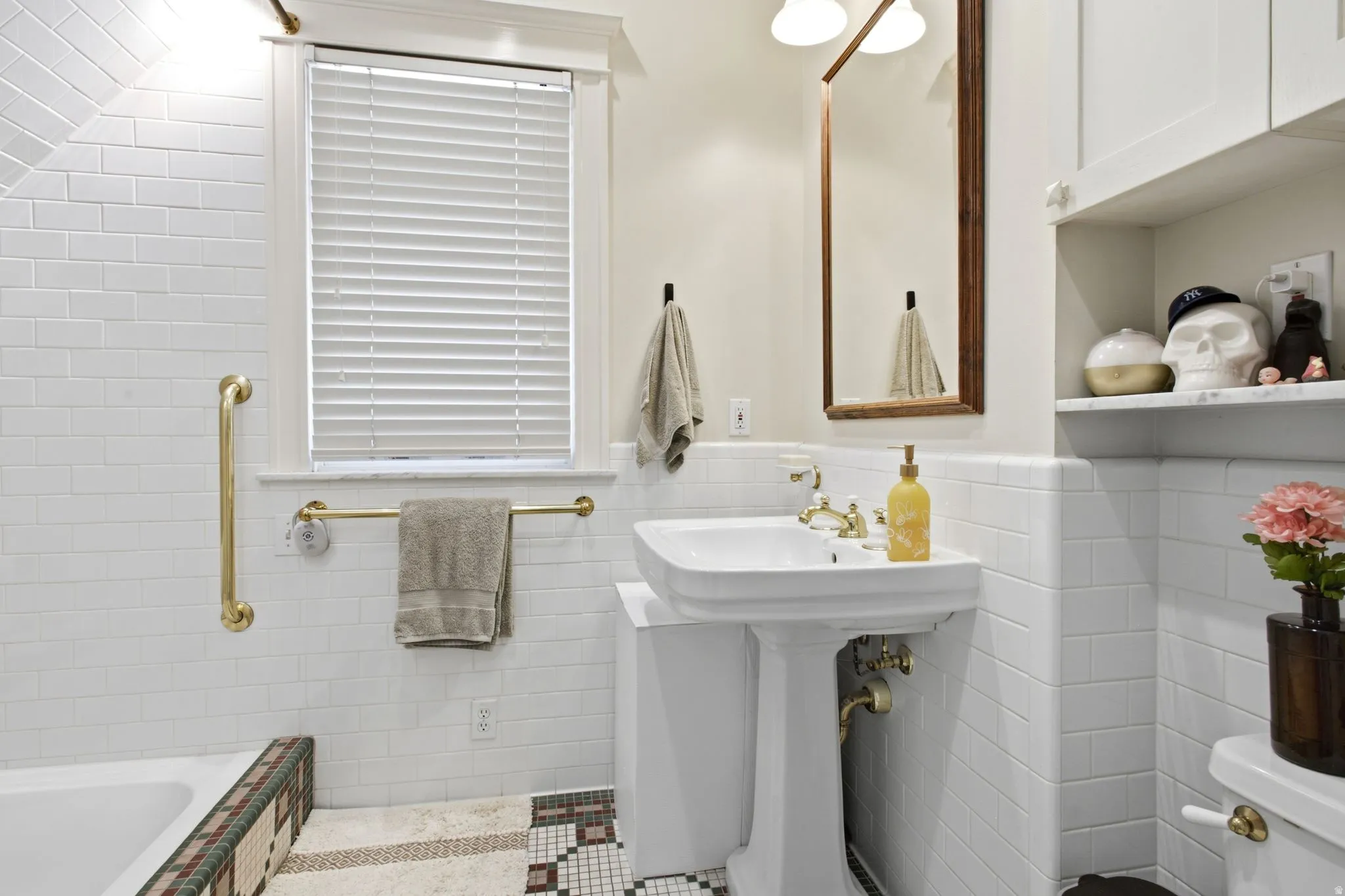 Bathroom featuring a white pedestal sink, subway tile walls, a wood-framed mirror, a built-in shelving unit, and a window with blinds