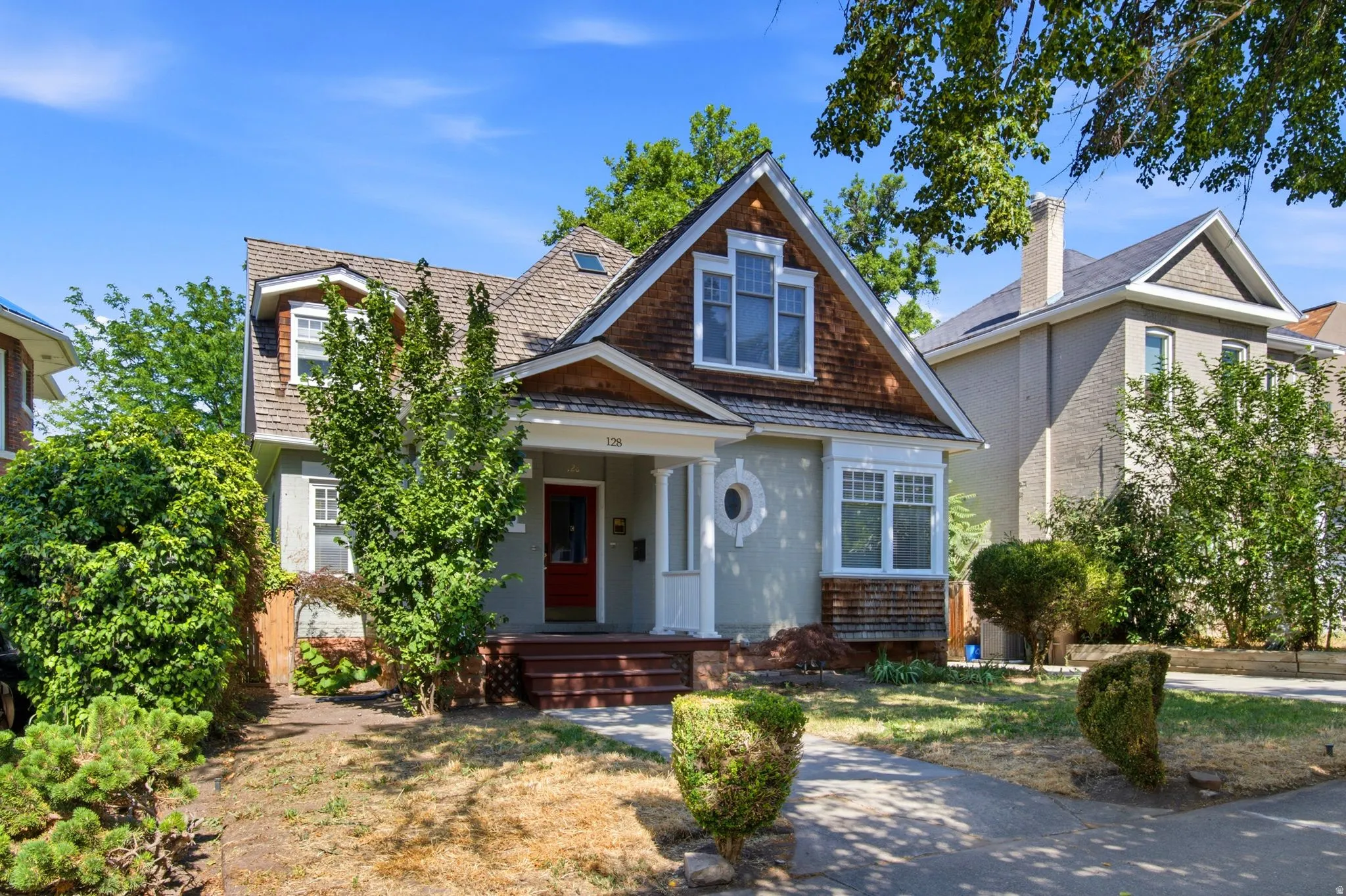 Craftsman-style home featuring a red entry door, shingle siding, dormer windows, and a covered porch