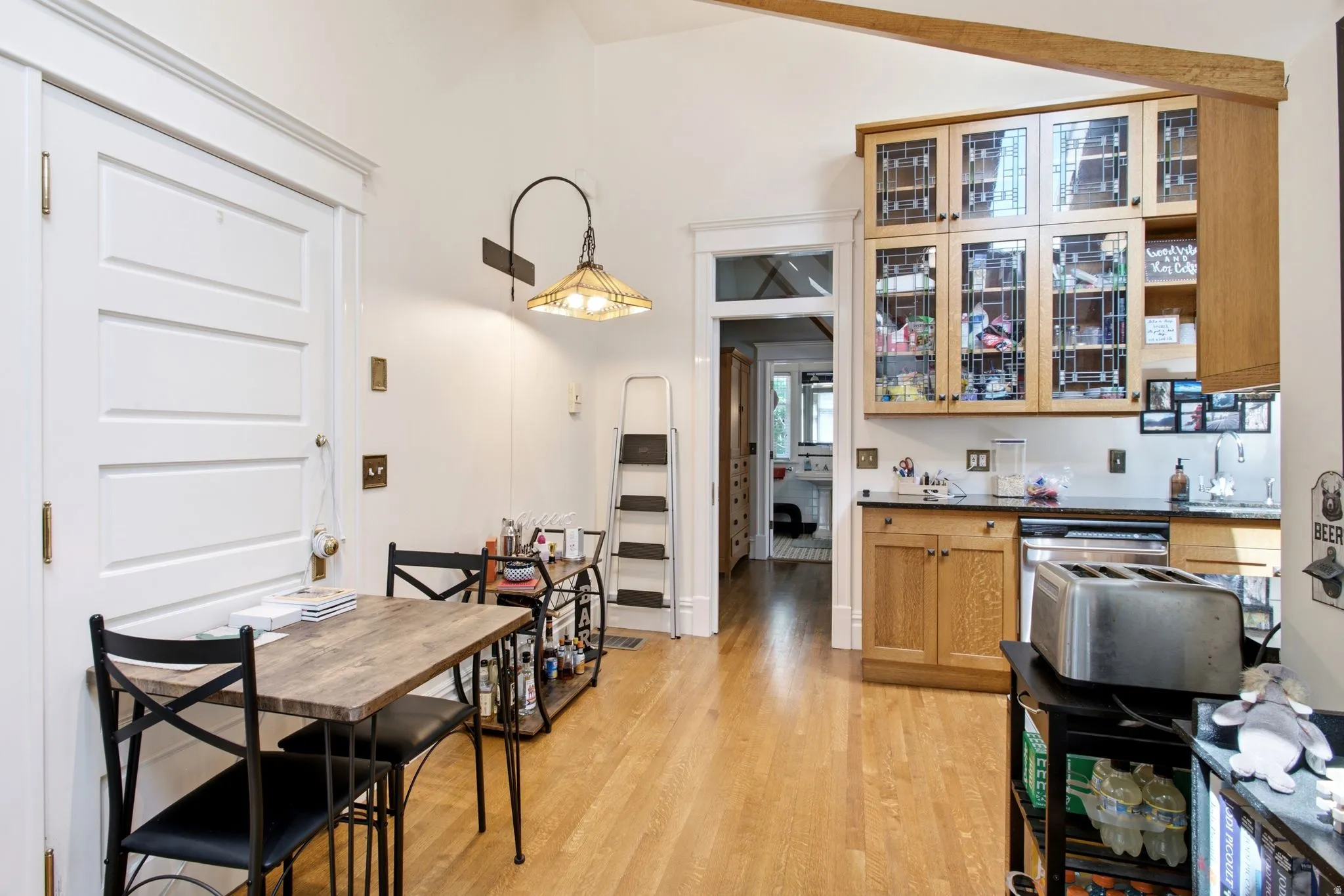 Kitchen area featuring wood-finish flooring, light-toned cabinetry with glass-front upper cabinets, and a built-in dishwasher