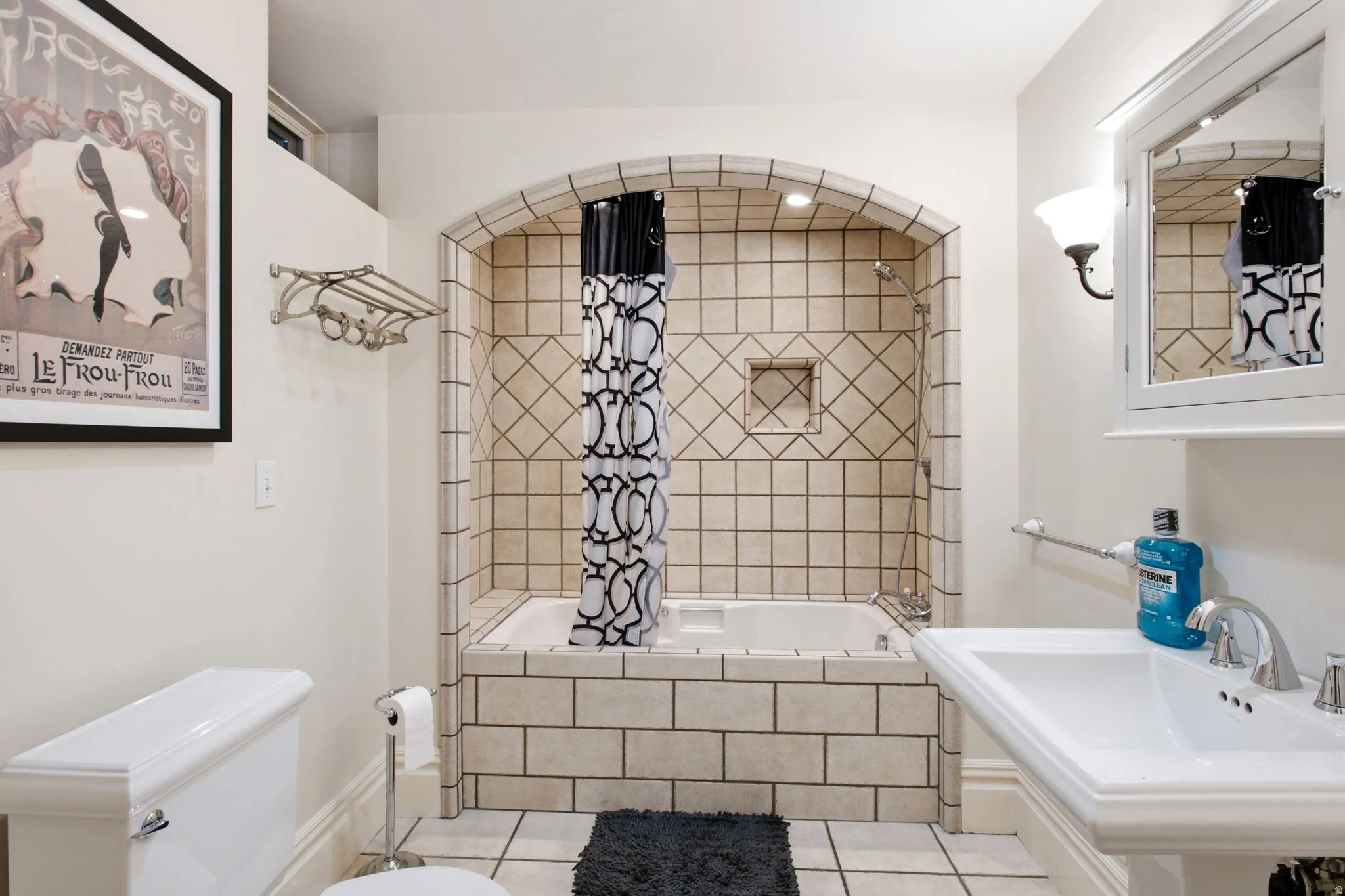 Bathroom featuring an arched tile shower enclosure with built-in niche, a pedestal sink with chrome faucet, a wall-mounted medicine cabinet, and ceramic tile flooring