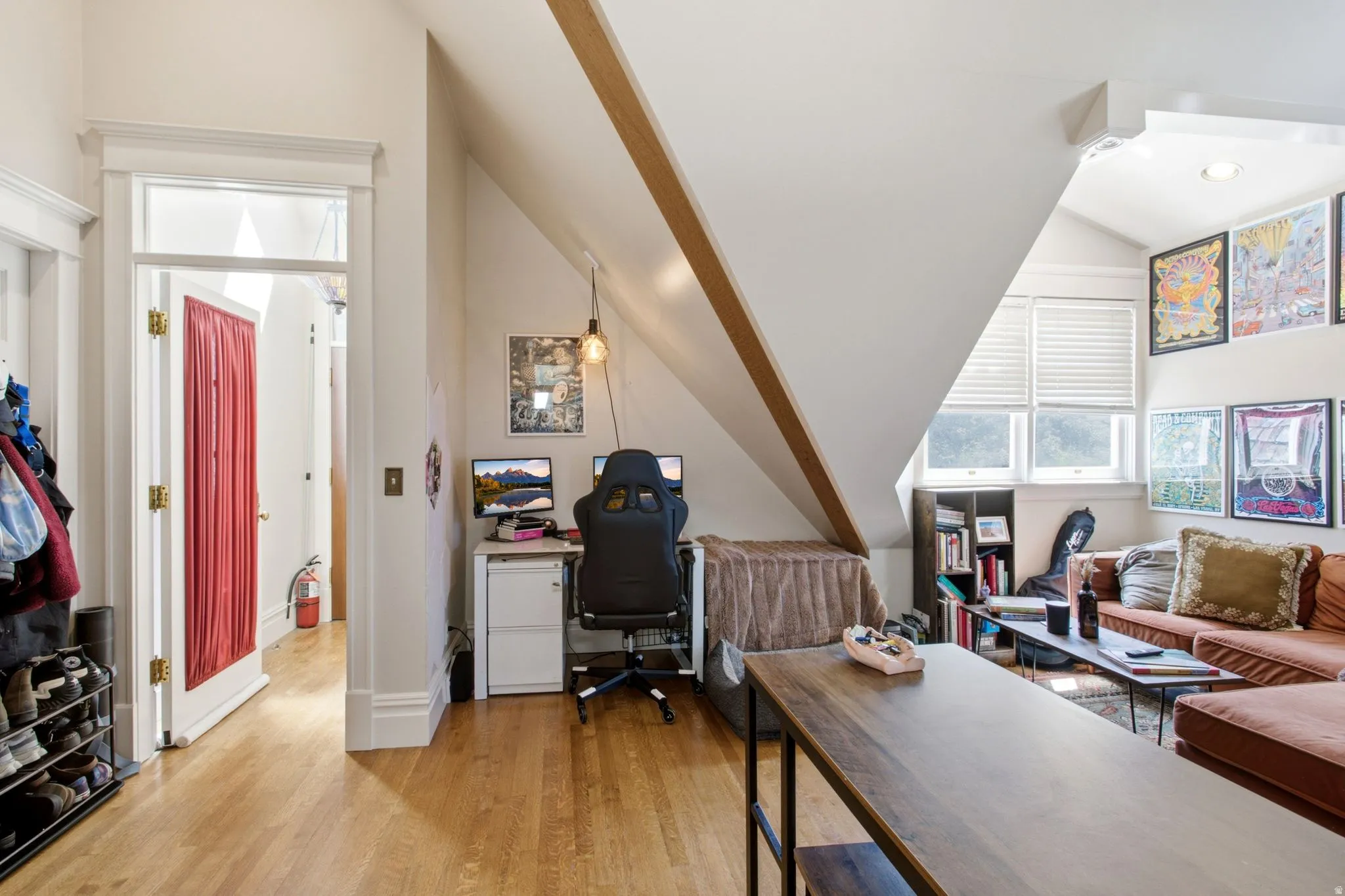 Hardwood flooring extends throughout this versatile attic space, featuring a sloped ceiling and exposed beam
