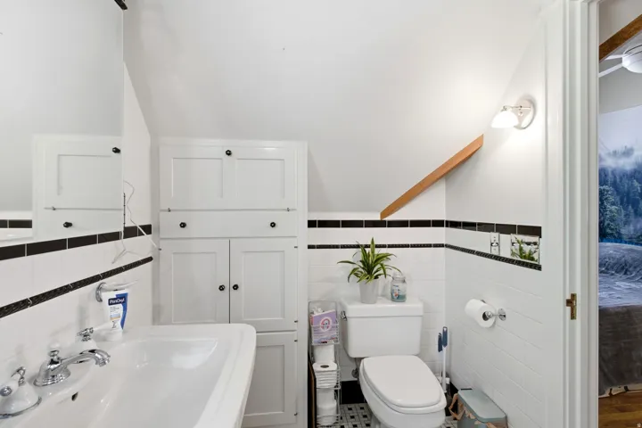 Bathroom featuring a pedestal sink with chrome fixtures, built-in white cabinetry, and white subway tile with black accent bands