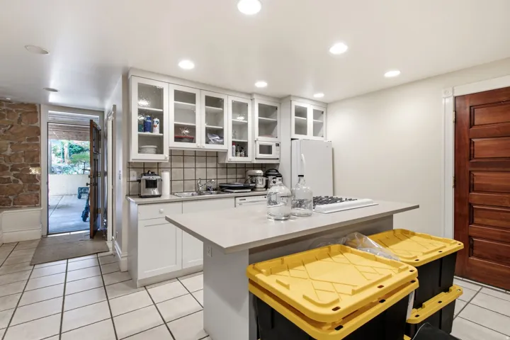 Kitchenette featuring white cabinetry with glass-front uppers, a light-toned countertop island with a built-in cooktop, and recessed lighting