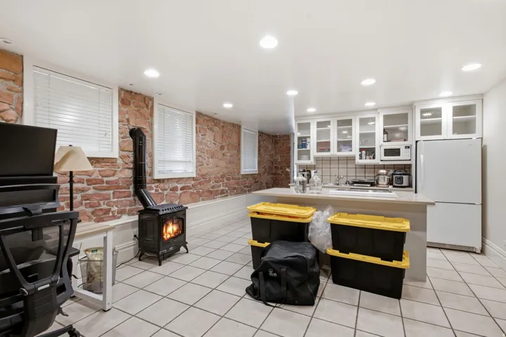 Finished basement space featuring exposed brick walls, a wood-burning stove, recessed lighting, and tile flooring