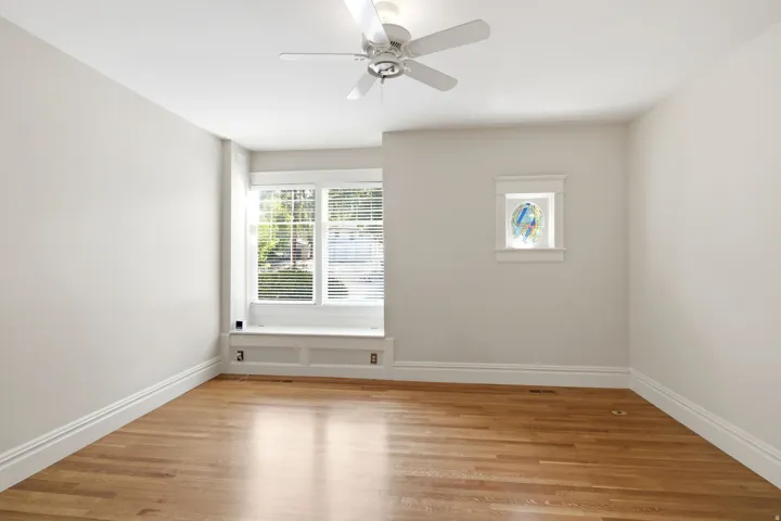 Bright interior space with wood-finish flooring, a window seat with paneling, a multi-pane window with blinds, a ceiling fan, and decorative trim around a smaller window