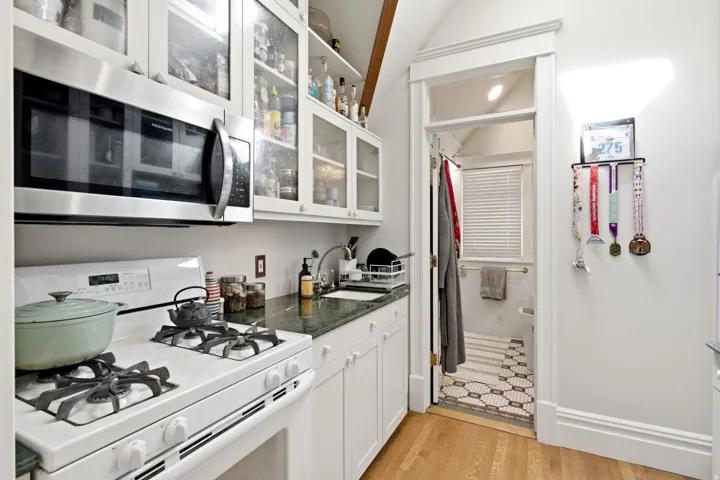 Kitchenette featuring white cabinetry with glass-front uppers, stainless steel microwave, white gas range, and dark countertop
