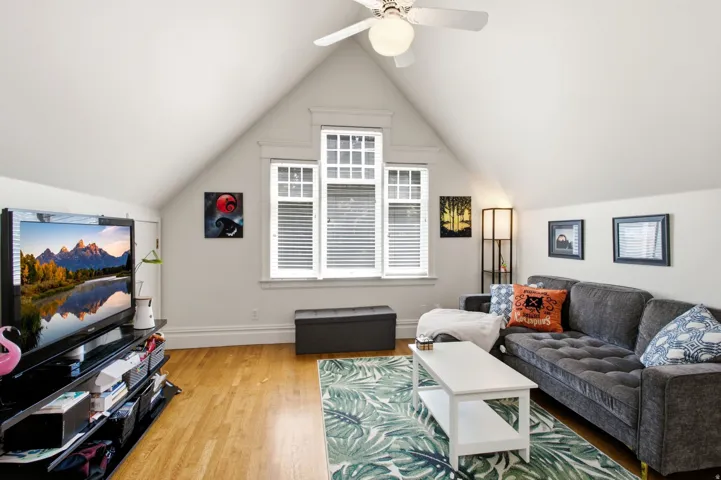 Attic living space featuring sloped ceilings, wood-finish flooring, and multiple windows with blinds