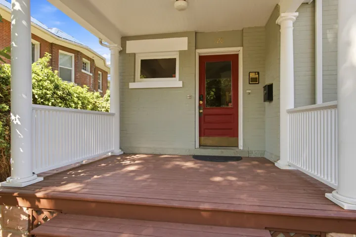Inviting covered porch with a red entry door, white columns, and wood-finish decking