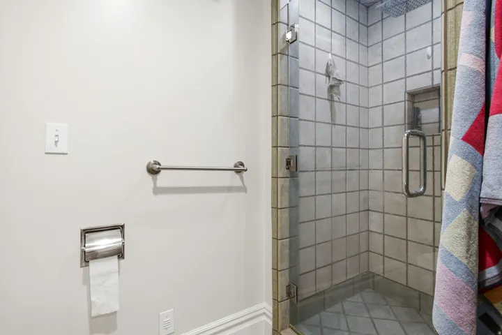 Glass-enclosed shower with square wall tiling, a built-in shelf, and a rain shower head