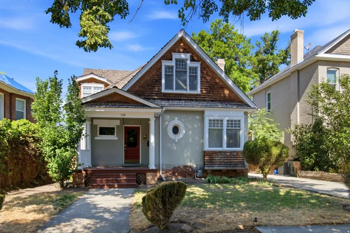 Craftsman-style home featuring a prominent gabled roof with wood shingle siding, a covered porch with white columns, and a red entry door