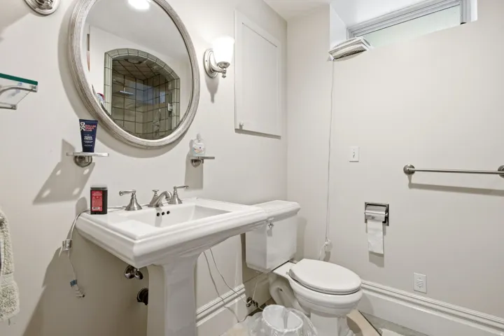 White pedestal sink with brushed nickel faucet, framed round mirror, and wall-mounted sconce lighting