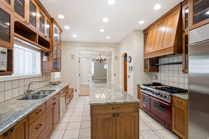 Kitchen featuring an expansive center island with granite countertop, wood-finish cabinetry, stainless steel appliances, and tile flooring